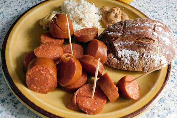 A Hasse (Burenwurst), a Beugel (Ende oder Anfang vom Brotlaib), a 16er Blech (eine Dose Ottakringer Bier). Dazu süßen und scharfen Senf und Kren. 